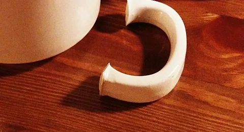 Foto enviada pela cliente: caneca com a alça quebrada, sobre uma mesa de madeira